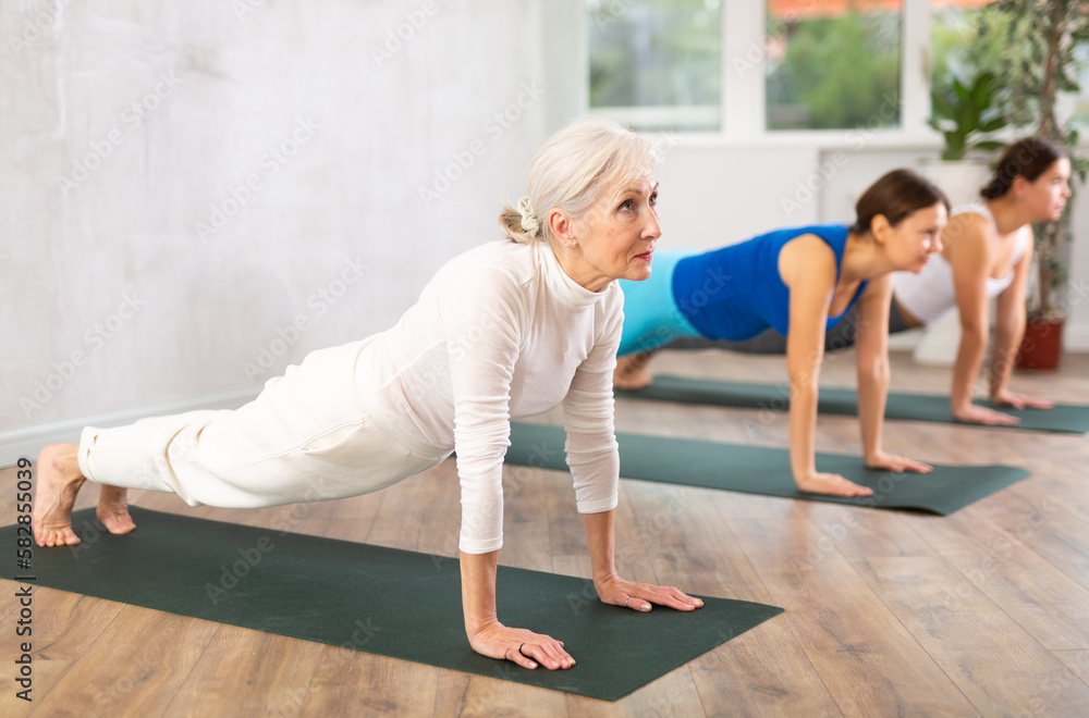 Elderly woman in sportswear performs fitness exercises in fitness center