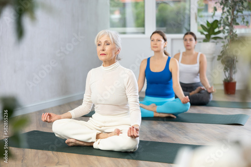 Elderly woman practicing yoga poses with other women in yoga studio