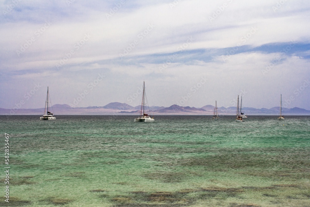 sailboats anchored on the island of la graciosa with the volcanoes of lanzarote in the background