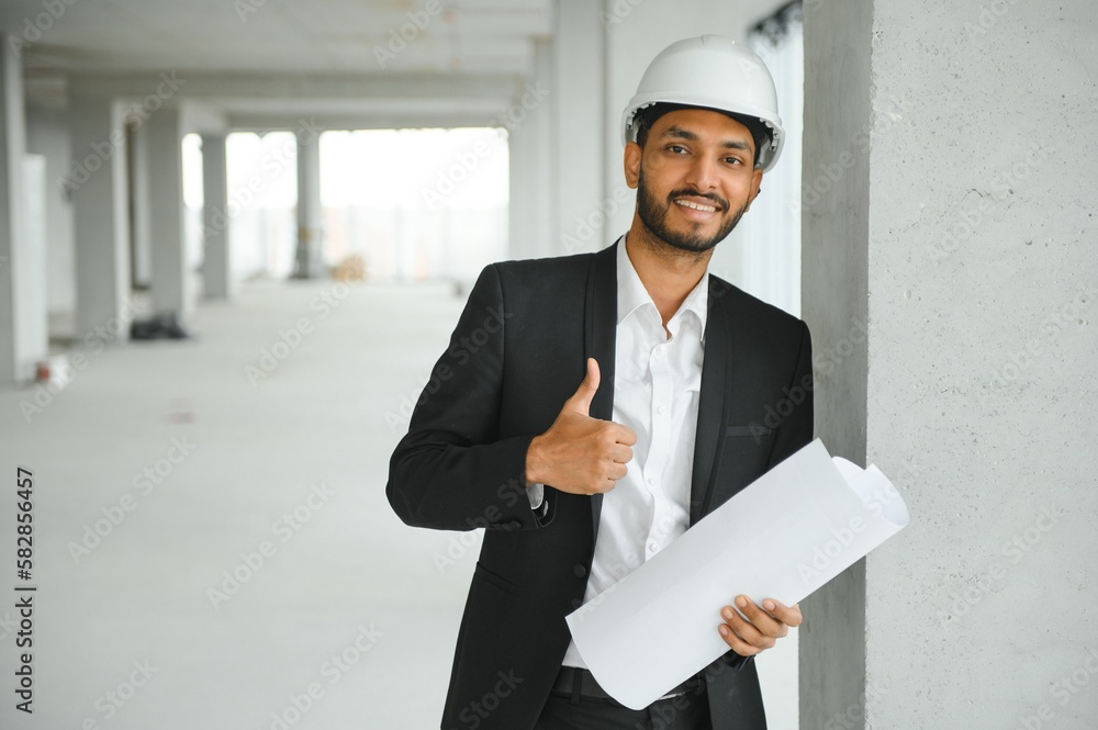 Indian construction site manager standing wearing helmet, thinking at construction site. Portrait of mixed race manual worker or architect.