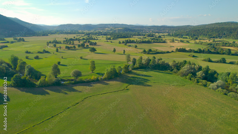 AERIAL Beautiful green fields with meandering river surrounded by forested hills