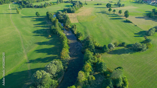 AERIAL: Meandering river, surrounded by lush greenery, winds through the fields