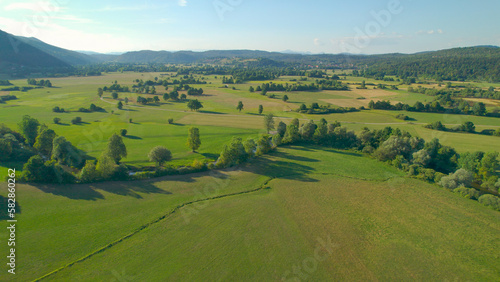 AERIAL Beautiful green fields with meandering river surrounded by forested hills