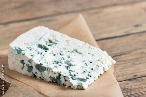 Slice of a blue cheese placed on a paper packaging with wooden background. Close up shot of a delicious blue cheese.