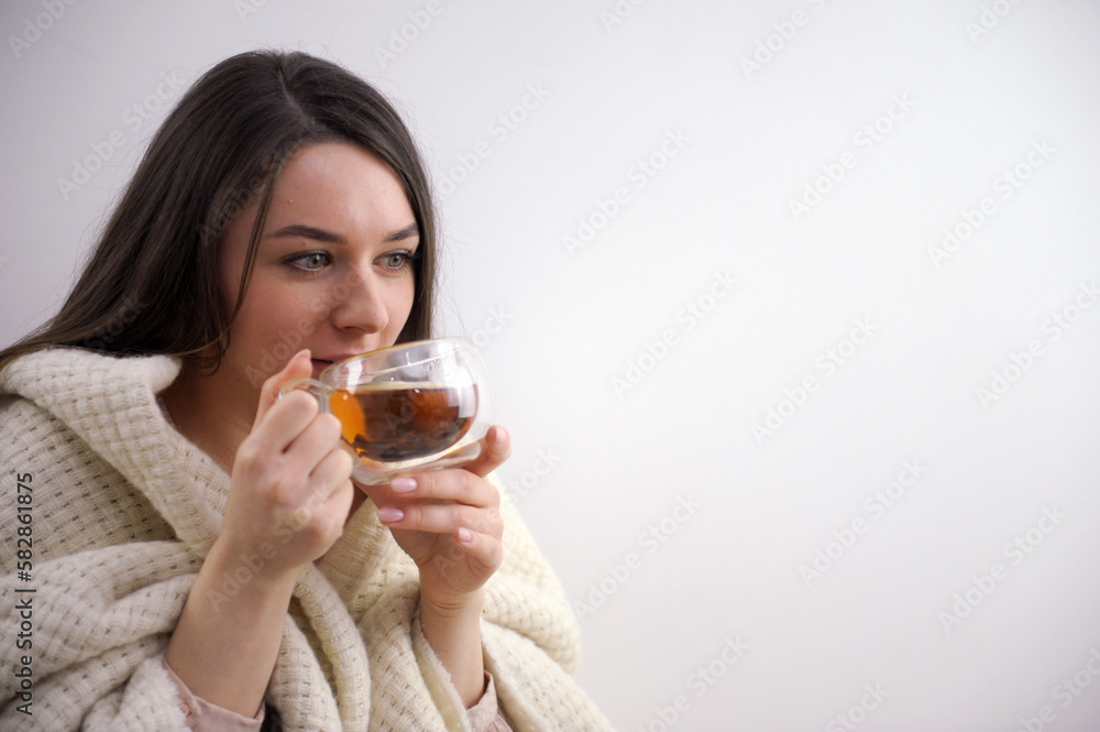 Cropped view of young adult woman covered in plaid, sitting near fireplace with fire and glass door in comfort house. Girl sitting at home with cup of beverage. High quality photo Cropped view of young adult woman covered in plaid, sitting near fireplace with fire and glass door in comfort house. Girl sitting at home with cup of beverage. High quality photo