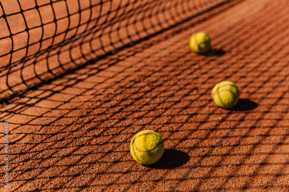 Light orange empty outdoor clay court surface dry grungy ground baseline detail for playing tennis with net shadow in sunny day, yellow green balls, gravel texture background, copy space for text 
 - obrazy, fototapety, plakaty 