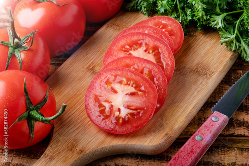 ripe tomato sliced with plastics and a knife on a cutting board. macro photography.