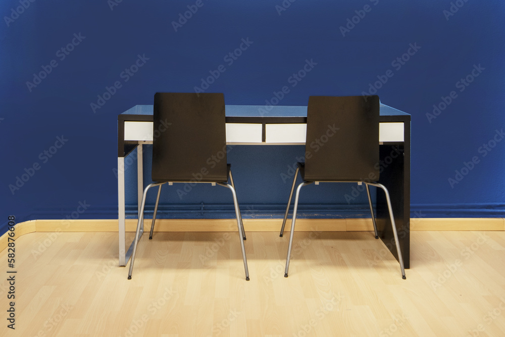 Obraz premium Study table attached to the simple blue black wall with metal legs and glass top with two black chairs