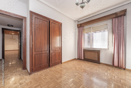 Empty living room of a house with a built-in wardrobe with sapele wood doors, a wooden radiator cover and a window with sheers and curtains photo