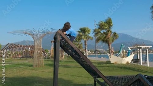 Children trampoline on shore. A little girl climb on sportground on trampoline against green garden under sun. photo