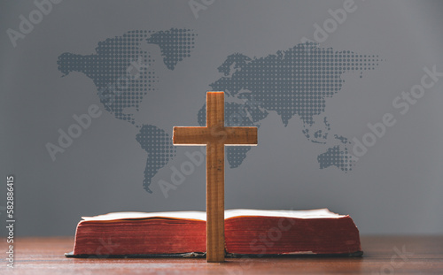 Cross with open Holy Bible on table with world map blur background. mission evangelism and gospel on world. Copy space for text, Christian background for great commission or earth day concept. photo