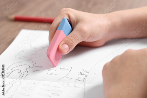 Girl erasing drawing in her book at wooden table, closeup