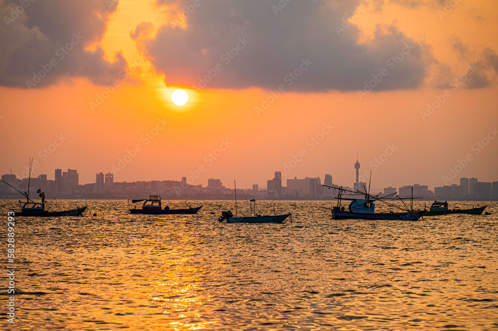Local fishing boats anchor in front of Koh Larn with Pattaya as the sun rises in the background, Thailand