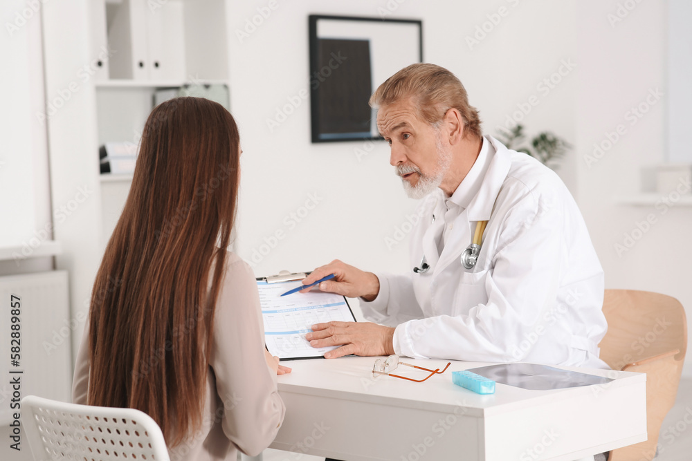 Professional orthopedist consulting patient at table in clinic Professional orthopedist consulting patient at table in clinic