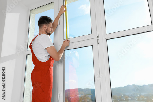 Obraz na plátně Worker in uniform measuring window with tape indoors