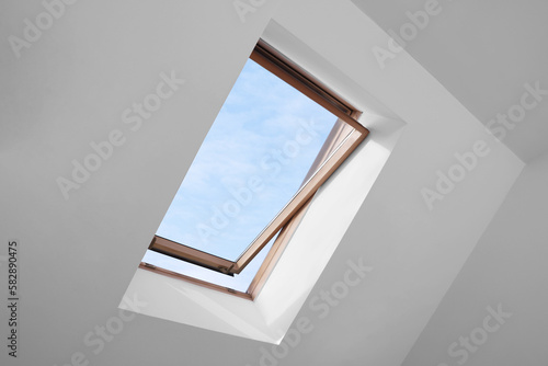 Foto Open skylight roof window and lamps on slanted ceiling in attic room, low angle