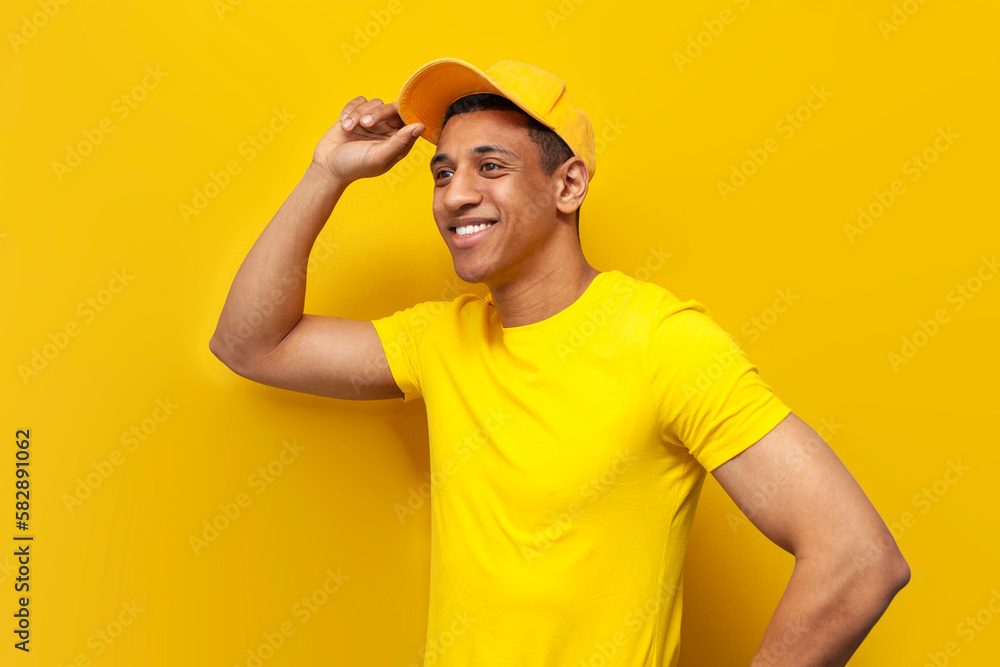 african american delivery man in yellow uniform stands on yellow background, service worker