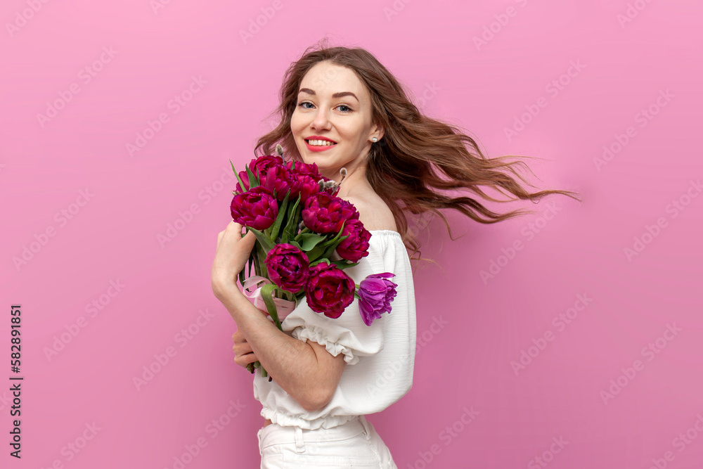 young attractive woman in white festive clothes holding bouquet of pink tulips and swirl on isolated background