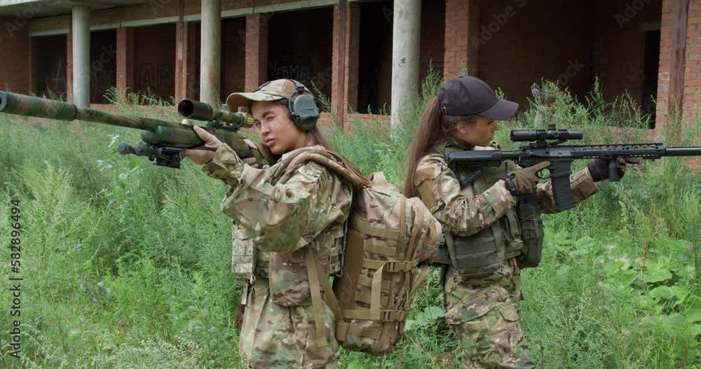 female soldiers with assault rifle aiming at viewer, standing back to back outdoors, women protecting, securing area, territory, side view camera motion female soldiers with assault rifle aiming at viewer, standing back to back outdoors, women protecting, securing area, territory, side view camera motion