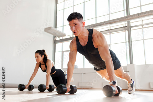 athletic couple in sportswear in training do push-ups with dumbbells in the fitness room in the morning