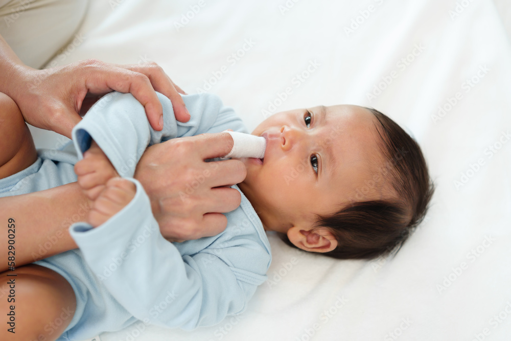 mother using finger to clean newborn baby mouth (tongue and gum) with clean gauze on bed - obrazy, fototapety, plakaty 