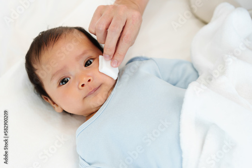 Foto mother cleaning and wiping newborn baby face with cotton pad on bed