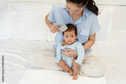 mother combing her newborn baby hair on bed