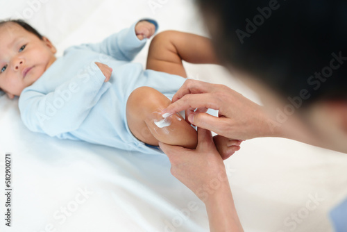 mother applying moisturizing cream on leg of newborn baby
