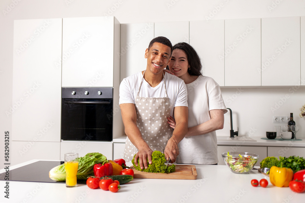 young happy multiracial couple preparing veggie vegetable and greens salad in white modern kitchen young happy multiracial couple preparing veggie vegetable and greens salad in white modern kitchen
