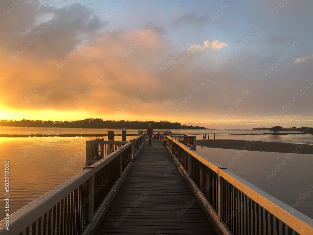 orange sunrise over still water with a man standing on a boardwalk  