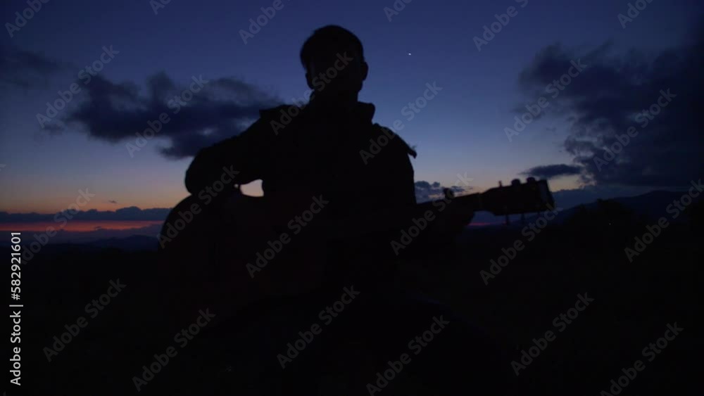 Silhouette of man playing the guitar at dusk with dramatic colors in the sky, Vietnam Silhouette of man playing the guitar at dusk with dramatic colors in the sky, Vietnam