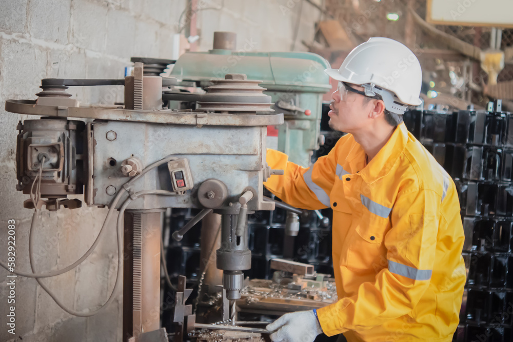 Engineer wearing yellow work clothes white hardhat and wear glove using drilling machine, Industry and production concept. Engineer wearing yellow work clothes white hardhat and wear glove using drilling machine, Industry and production concept.