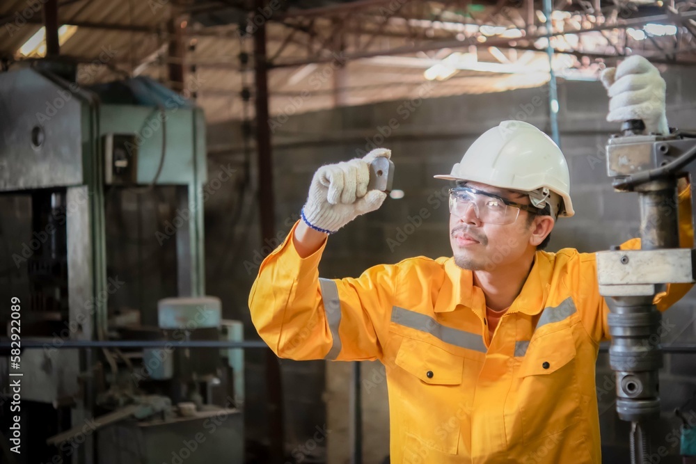 Engineer wearing yellow work clothes white hardhat and wear glove in close up shot holding material with drilling machine with serious face, Industry and production concept. Engineer wearing yellow work clothes white hardhat and wear glove in close up shot holding material with drilling machine with serious face, Industry and production concept.
