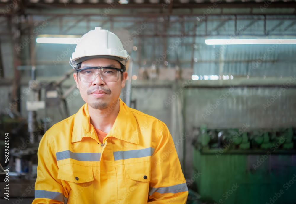 Asian professional engineer wearing yellow work clothes glasses and wear glove in close up shot looking to the camera in the industrial factory, Industry and production concept. Asian professional engineer wearing yellow work clothes glasses and wear glove in close up shot looking to the camera in the industrial factory, Industry and production concept.