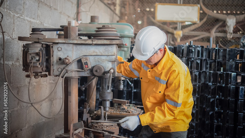 Engineer wearing yellow work clothes white hardhat and wear glove using drilling machine.