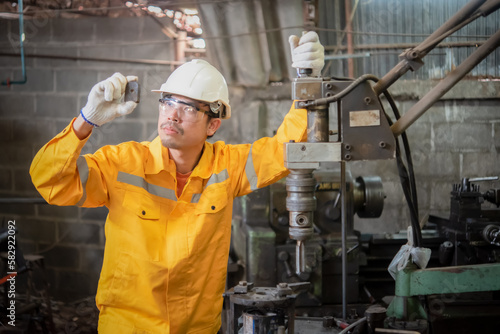 Engineer wearing yellow work clothes white hardhat and wear glove holding material with drilling machine with serious face, Industry and production concept.