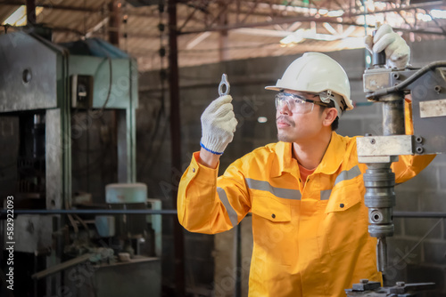 Engineer wearing yellow work clothes white hardhat and wear glove holding material with drilling machine, Industry and production concept.