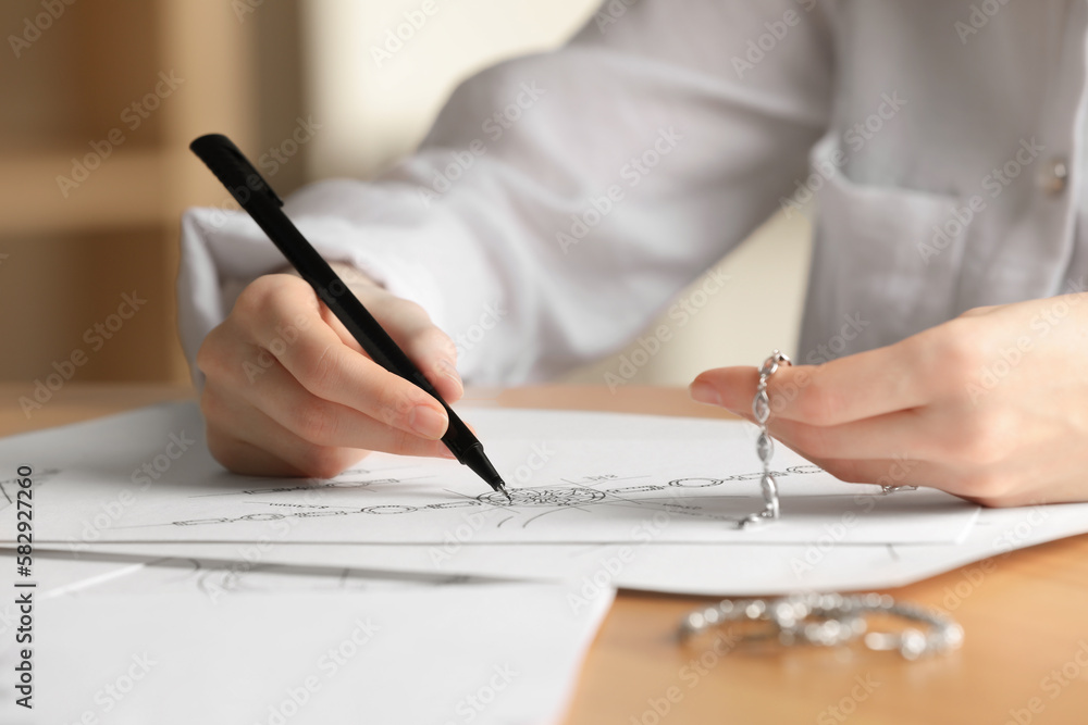 Jeweler drawing sketch of elegant bracelet on paper at wooden table indoors, closeup Jeweler drawing sketch of elegant bracelet on paper at wooden table indoors, closeup