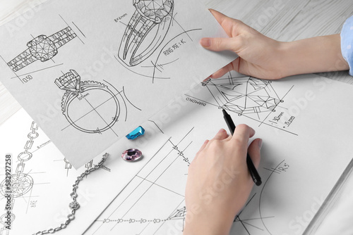 Jeweler with sketches of elegant jewelry at white wooden table, closeup photo