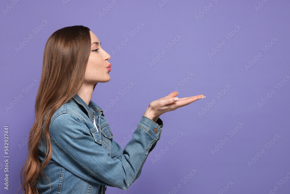 Beautiful young woman blowing kiss on purple background, space for text Beautiful young woman blowing kiss on purple background, space for text
