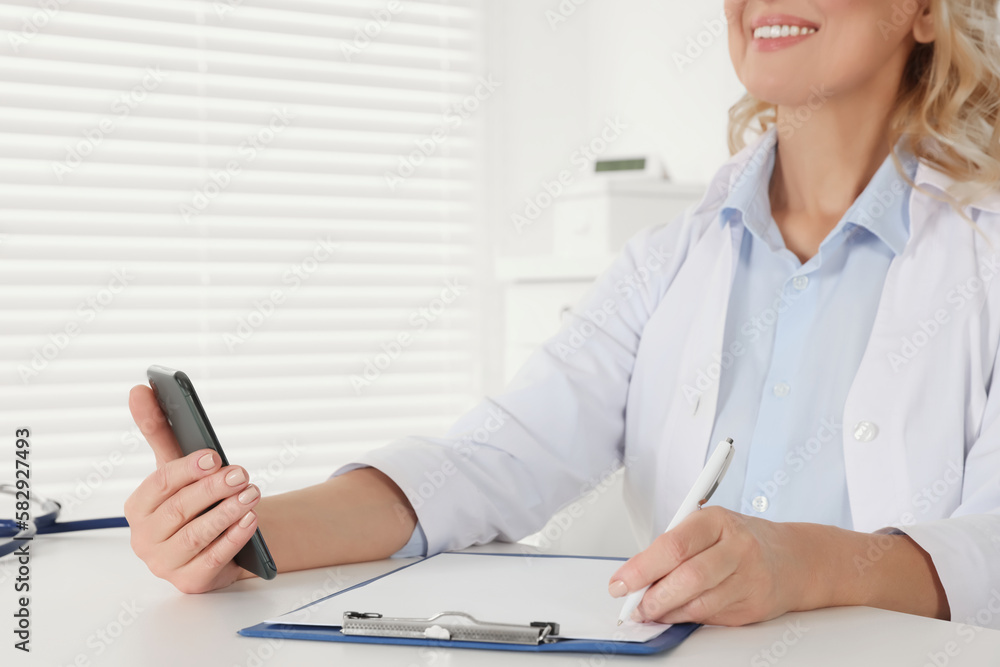Doctor with smartphone and clipboard at desk in clinic, closeup. Online medicine concept Doctor with smartphone and clipboard at desk in clinic, closeup. Online medicine concept