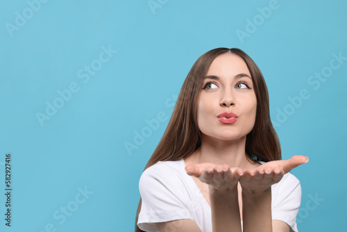 Beautiful young woman blowing kiss on light blue background, space for text