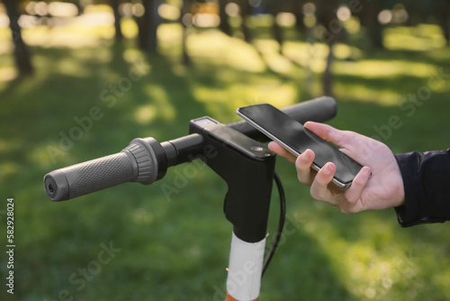 Man using smartphone to pay and unblock rental electric scooter outdoors, closeup