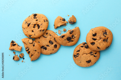 Many delicious chocolate chip cookies on light blue background, flat lay
