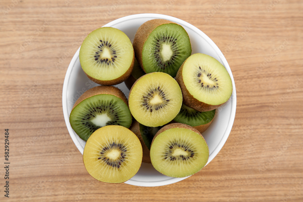 Bowl of many cut fresh kiwis on wooden table, top view Bowl of many cut fresh kiwis on wooden table, top view