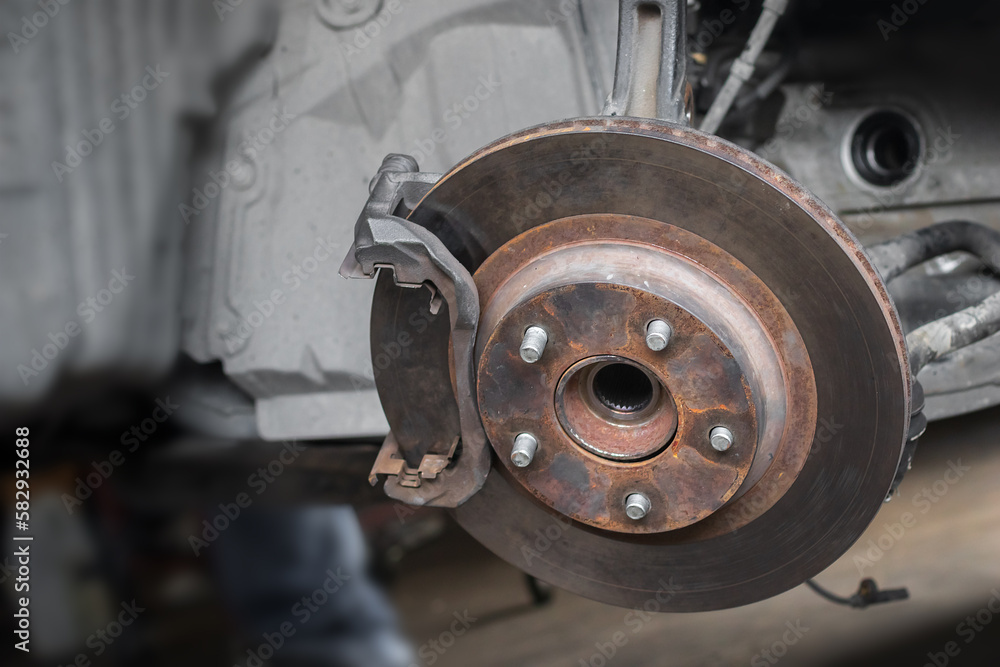 Close-up rusty disk break and wheel hub of 4x4 car waiting check list for repair or maintenance with blurry mechanical fitter working in the garage shop background. Selective focus. Close-up rusty disk break and wheel hub of 4x4 car waiting check list for repair or maintenance with blurry mechanical fitter working in the garage shop background. Selective focus.