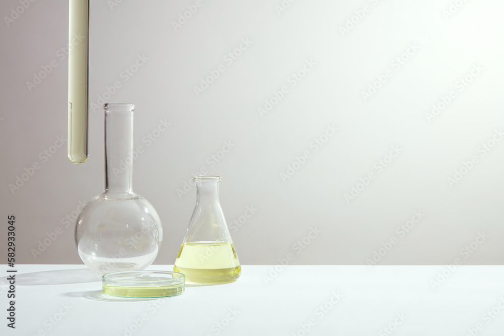 Science and medical background with boiling flask, erlenmeyer flask, petri dish and test tube containing yellow liquid on white background. Space for text and design. Science and medical background with boiling flask, erlenmeyer flask, petri dish and test tube containing yellow liquid on white background. Space for text and design.