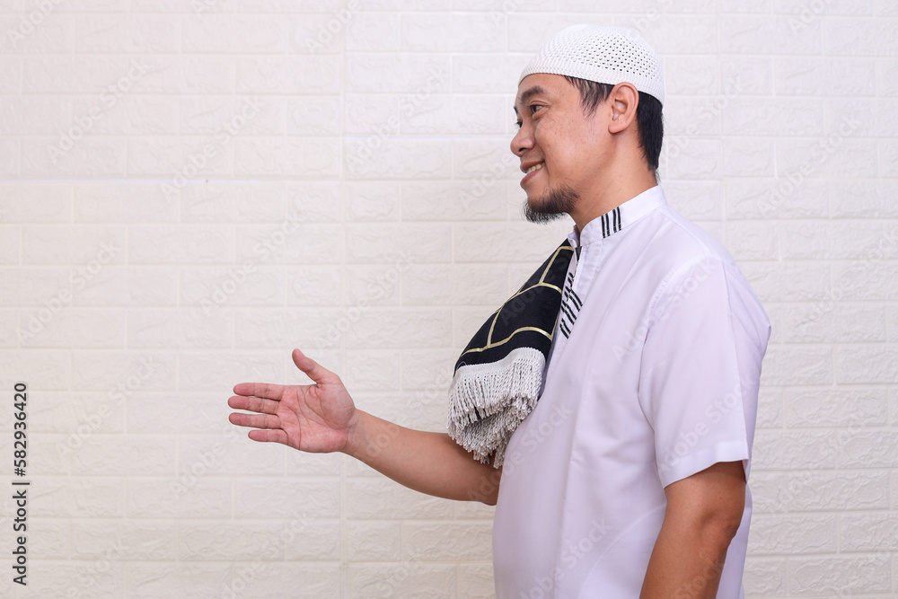 Muslim Asian man smiling friendly while offering a handshake over white background Muslim Asian man smiling friendly while offering a handshake over white background