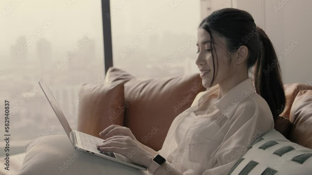 Smiling focused young woman chatting on laptop pc sitting on couch at living room. Happy modern freelancer female working remotely use computer at home. Smiling focused young woman chatting on laptop pc sitting on couch at living room. Happy modern freelancer female working remotely use computer at home.