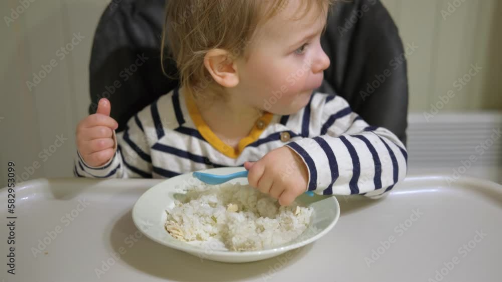 Young Kid Eating Blend Mashed Feed Sitting in High Chair. Baby Weaning. Little Girl Learning to Eat Yogurt, Feeding Himself. Small Hand with Spoon. Breakfast with Dairy Product. Child First Solid Food Young Kid Eating Blend Mashed Feed Sitting in High Chair. Baby Weaning. Little Girl Learning to Eat Yogurt, Feeding Himself. Small Hand with Spoon. Breakfast with Dairy Product. Child First Solid Food